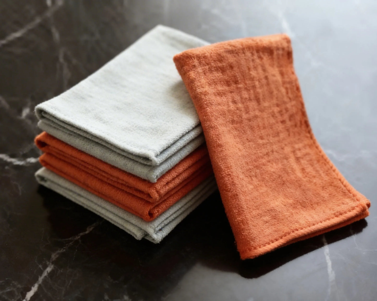 Stack of folded orange and gray cloths on a marble surface