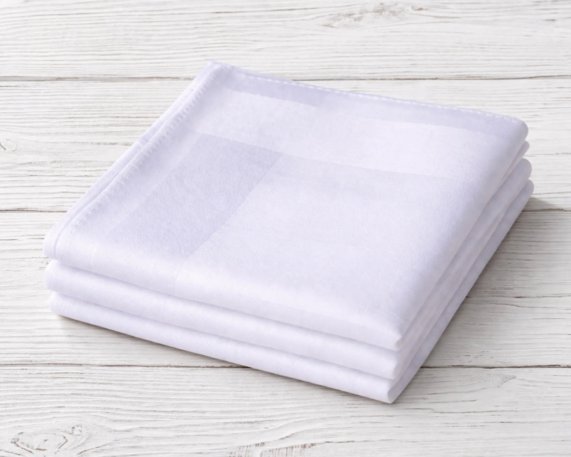 Stack of white folded towels on a light wooden surface