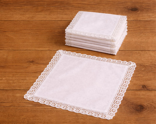 Stack of white lace-trimmed handkerchiefs on a wooden surface