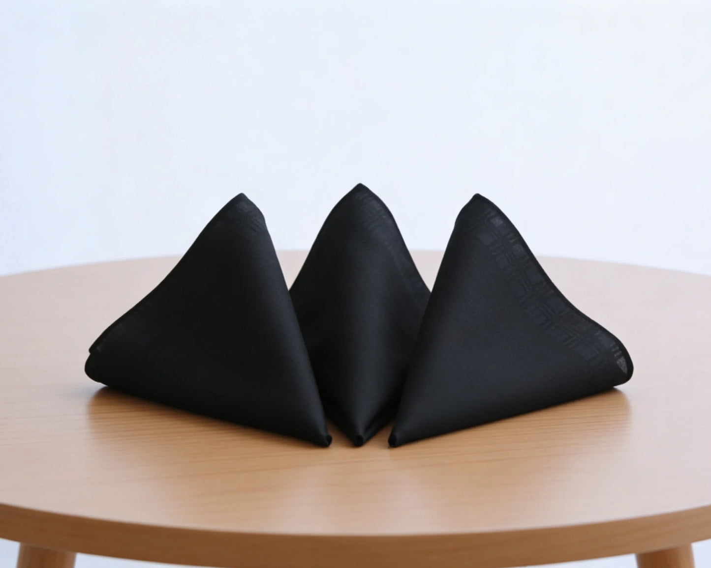 Three black triangular hanky on a wooden table with a light blue background