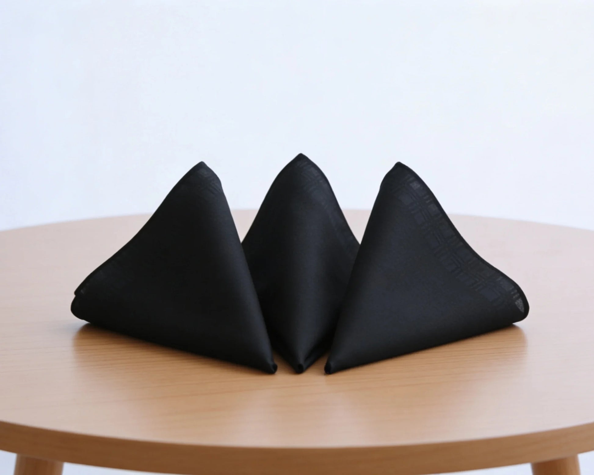 Three black triangular hanky on a wooden table with a light blue background