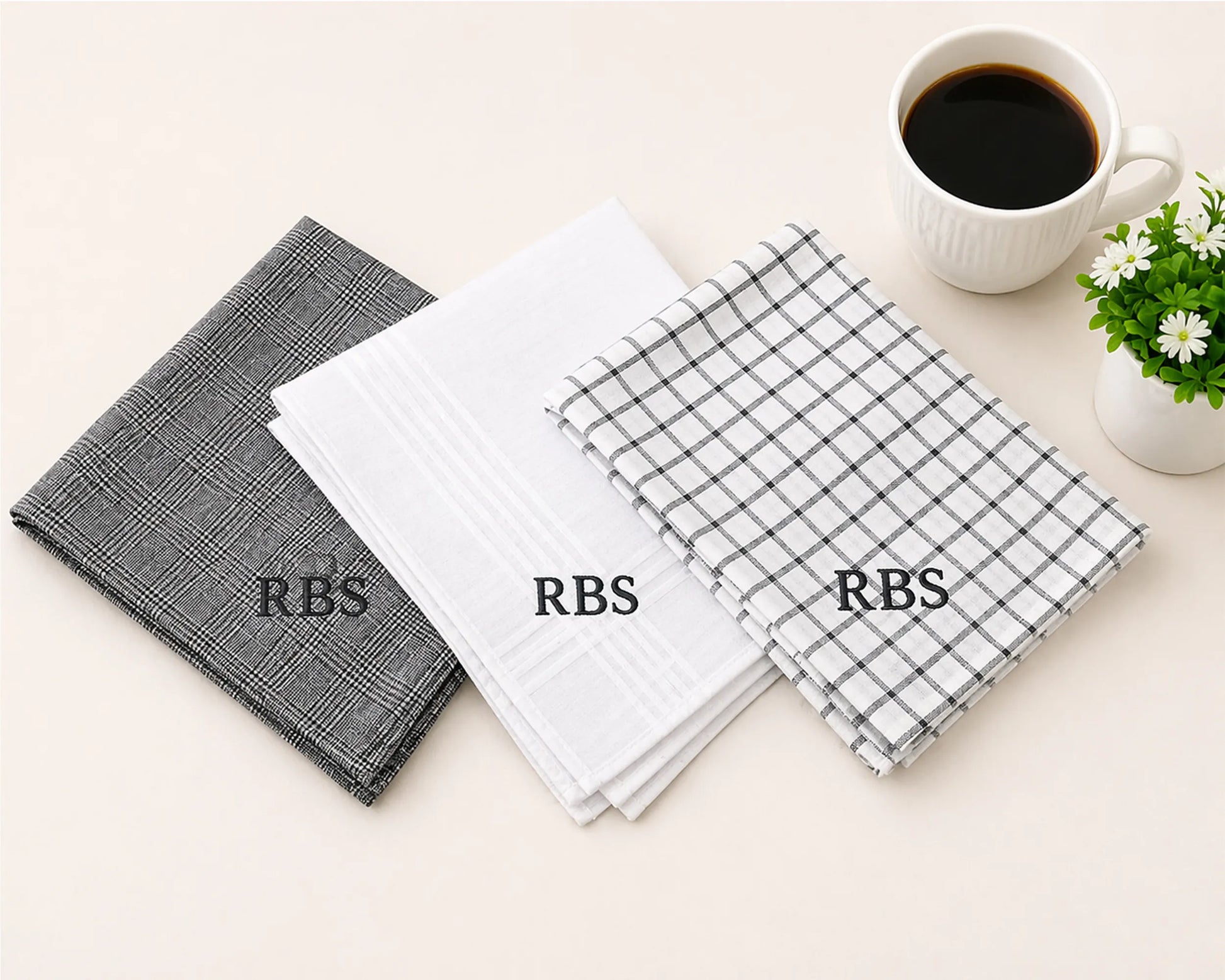 Three checkered hanky with 'RBS' branding on a light surface with a cup of coffee and plant.