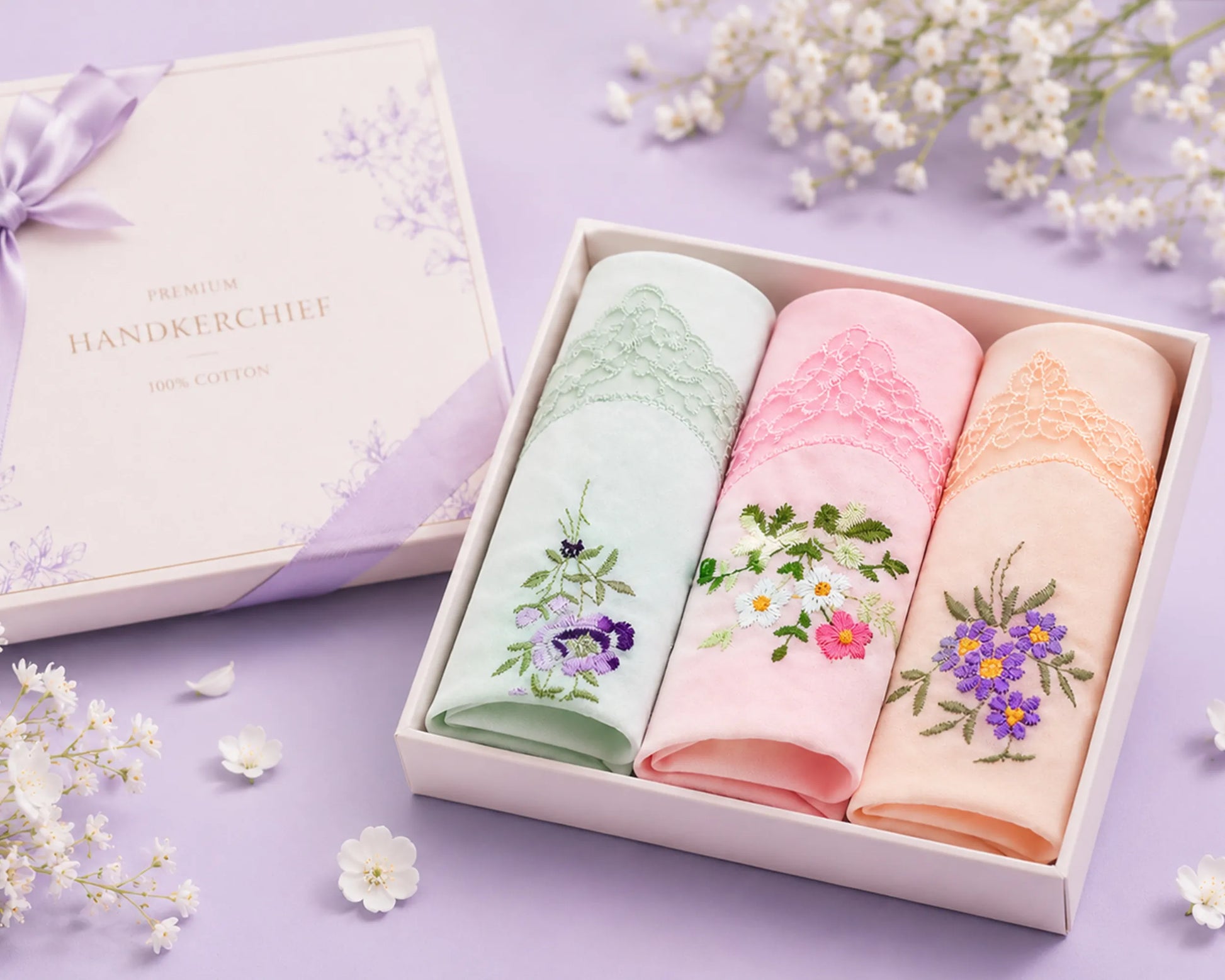 Three floral embroidered handkerchiefs in a box on a purple background with flowers.