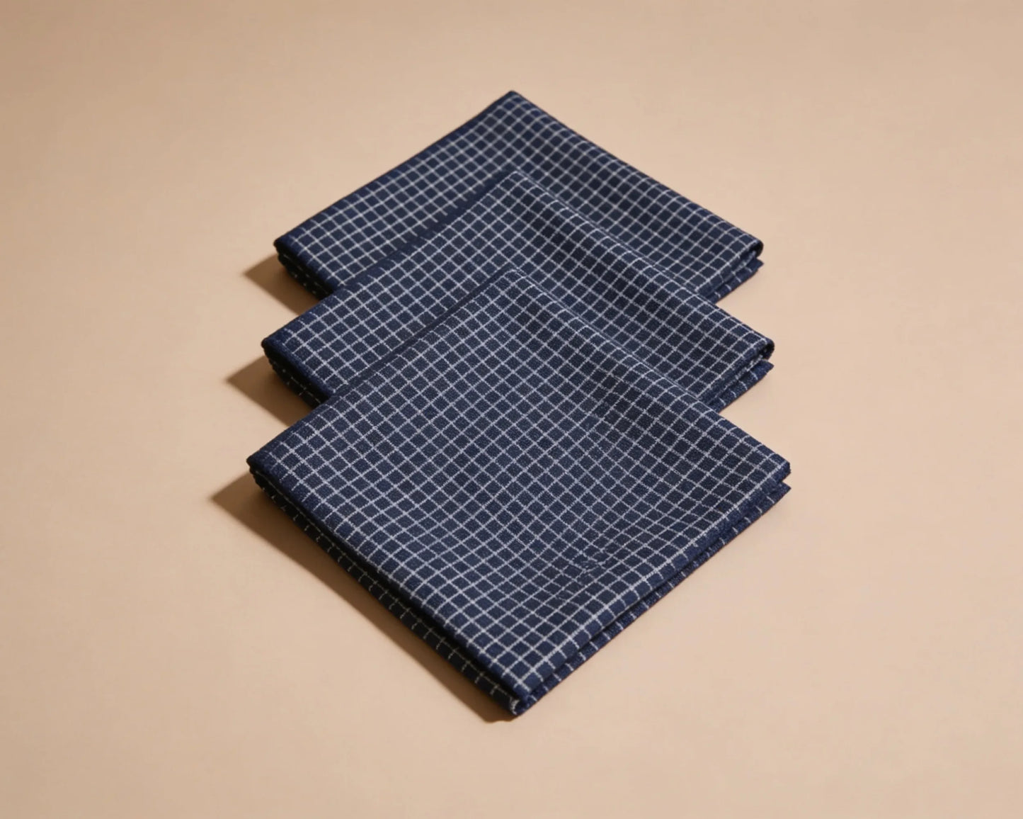 Three folded blue checkered hanky on a beige background