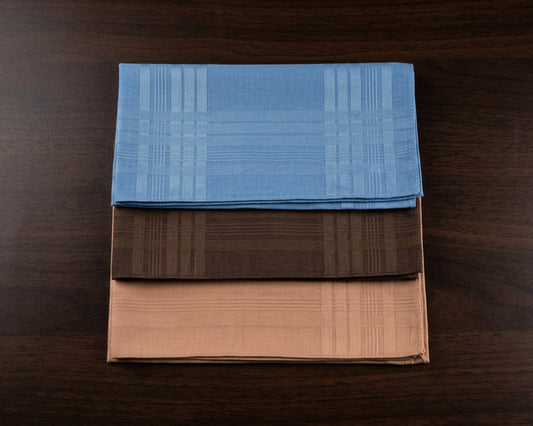 Three folded cotton hanky in blue, brown, and beige on a wooden surface