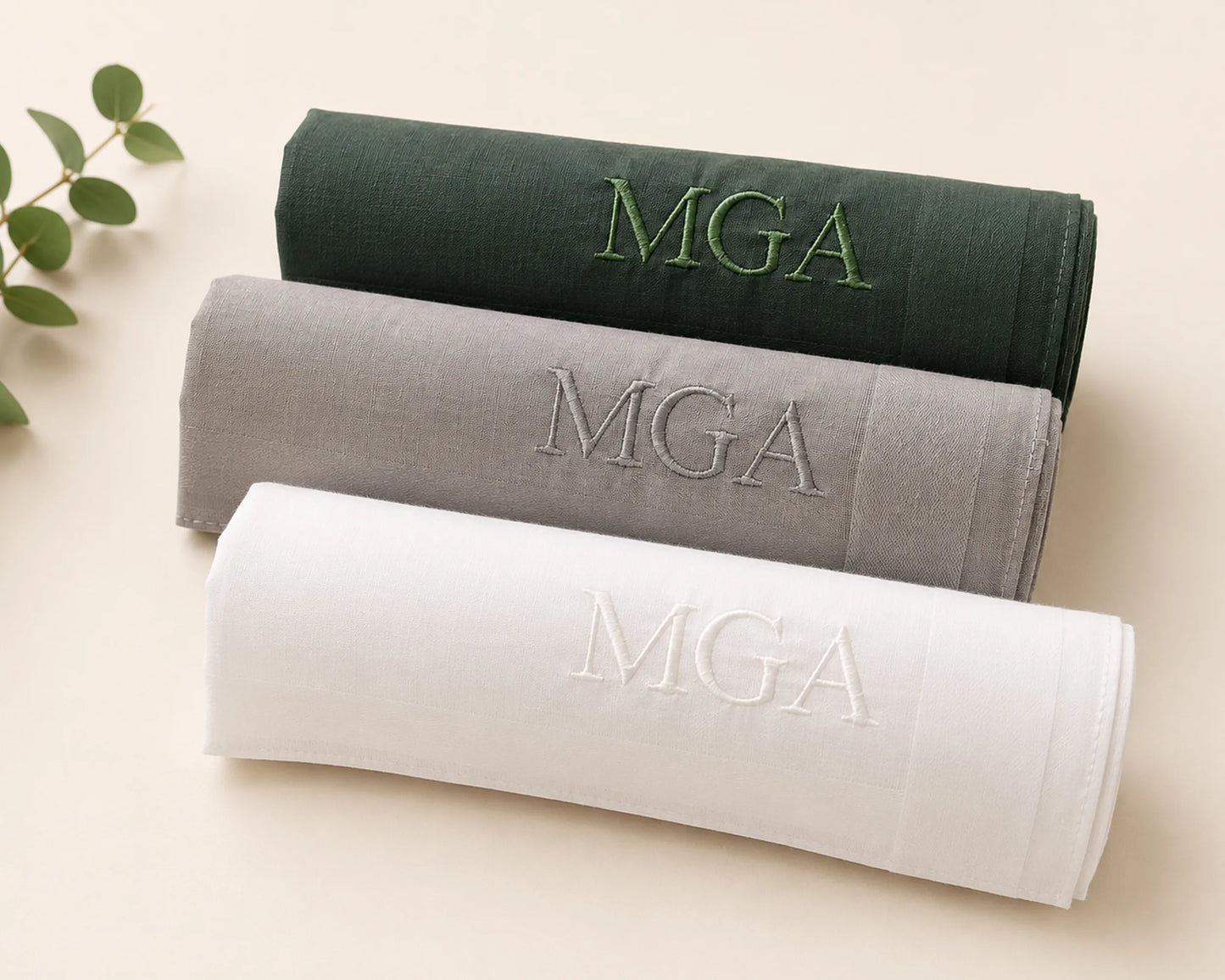 Three folded hankie in green, gray, and white with 'MGA' embroidery on a beige background.