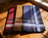 Three folded fabric swatches in red, brown, and blue plaid on a wooden surface.