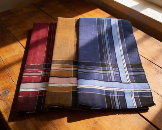 Three folded fabric swatches in red, brown, and blue plaid on a wooden surface.