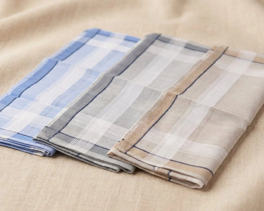 Three folded plaid hanky in blue, gray, and beige on a beige fabric background