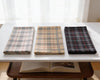 Three folded plaid fabrics on a white table with an open book underneath.