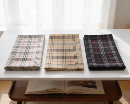 Three folded plaid fabrics on a white table with an open book underneath.