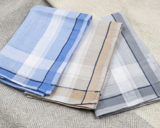 Three folded plaid napkins in blue, beige, and gray on a textured surface.