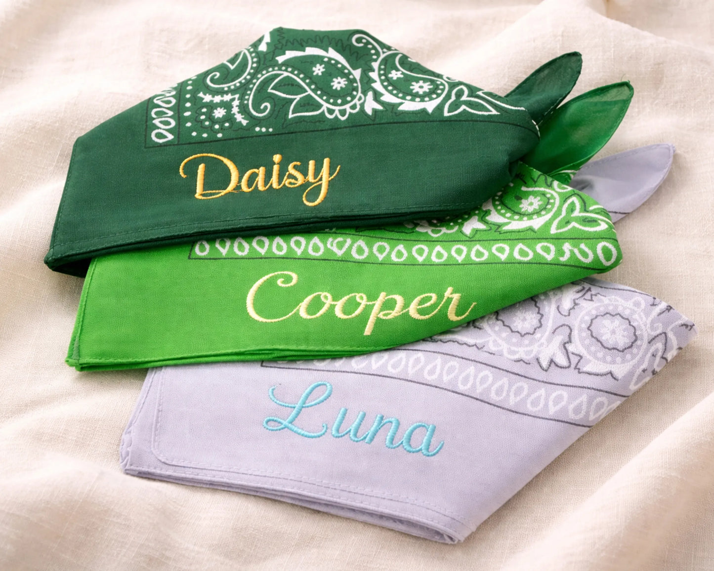Three green bandanas with embroidered names on a beige surface