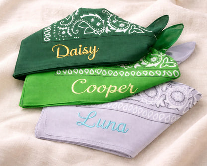 Three green bandanas with embroidered names on a beige surface