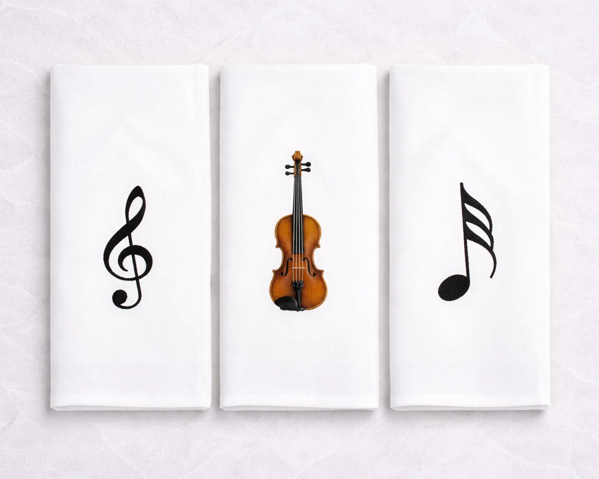 Three hanky artworks featuring musical symbols and a violin on a white wall.