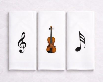 Three hanky artworks featuring musical symbols and a violin on a white wall.