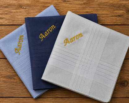 Three hanky  with 'Aaron' embroidered on them, stacked on a wooden surface.