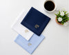 Three monogrammed pocket squares on a white surface with a cup of coffee and small plant.