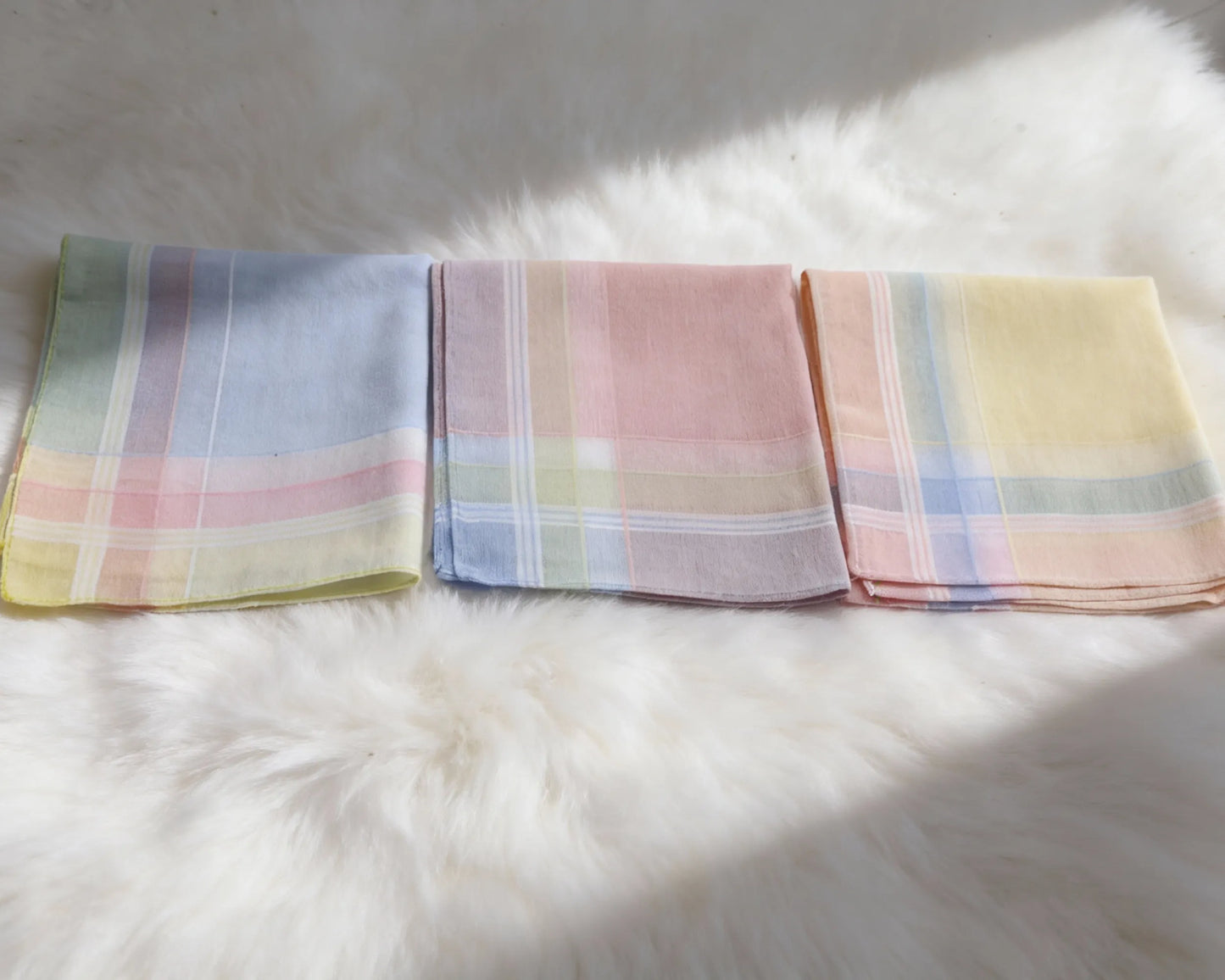 Three pastel colored plaid handkerchiefs on a white fur surface