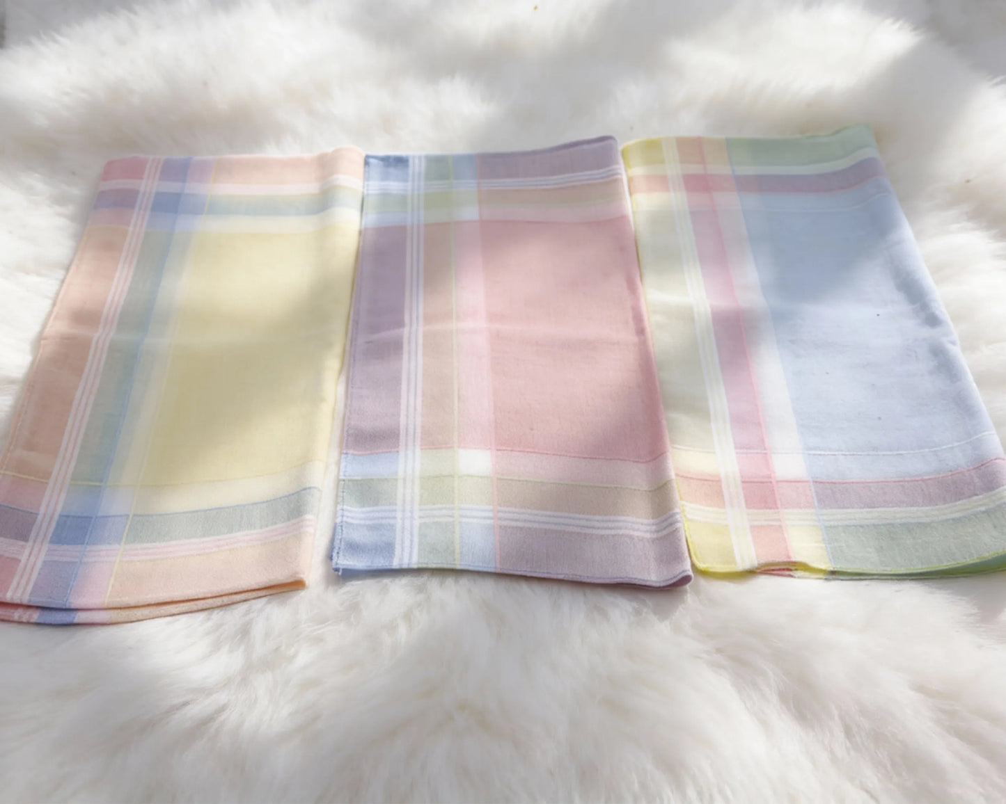 Three pastel plaid handkerchiefs on a white fur surface
