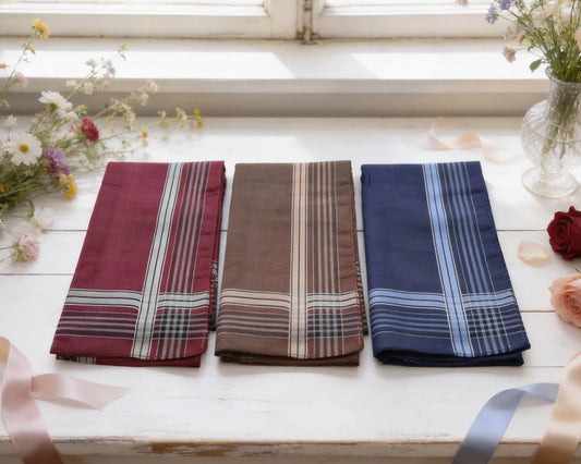 Three plaid hanky in red, brown, and blue on a white surface with flowers and ribbons.