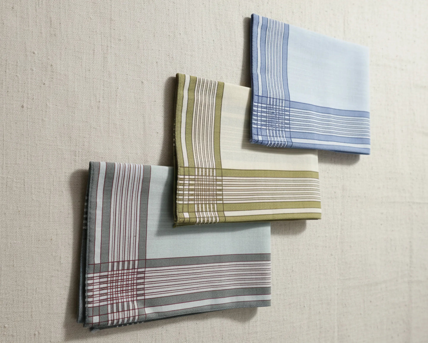 Three plaid handkerchiefs in different patterns on a textured beige background