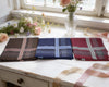 Three plaid pocket squares on a wooden surface with flowers in the background