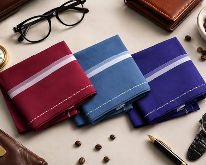 Three pocket squares in red, blue, and purple with white stripes on a surface with accessories.