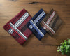 Three striped pocket squares on a wooden surface with a plant in the corner.