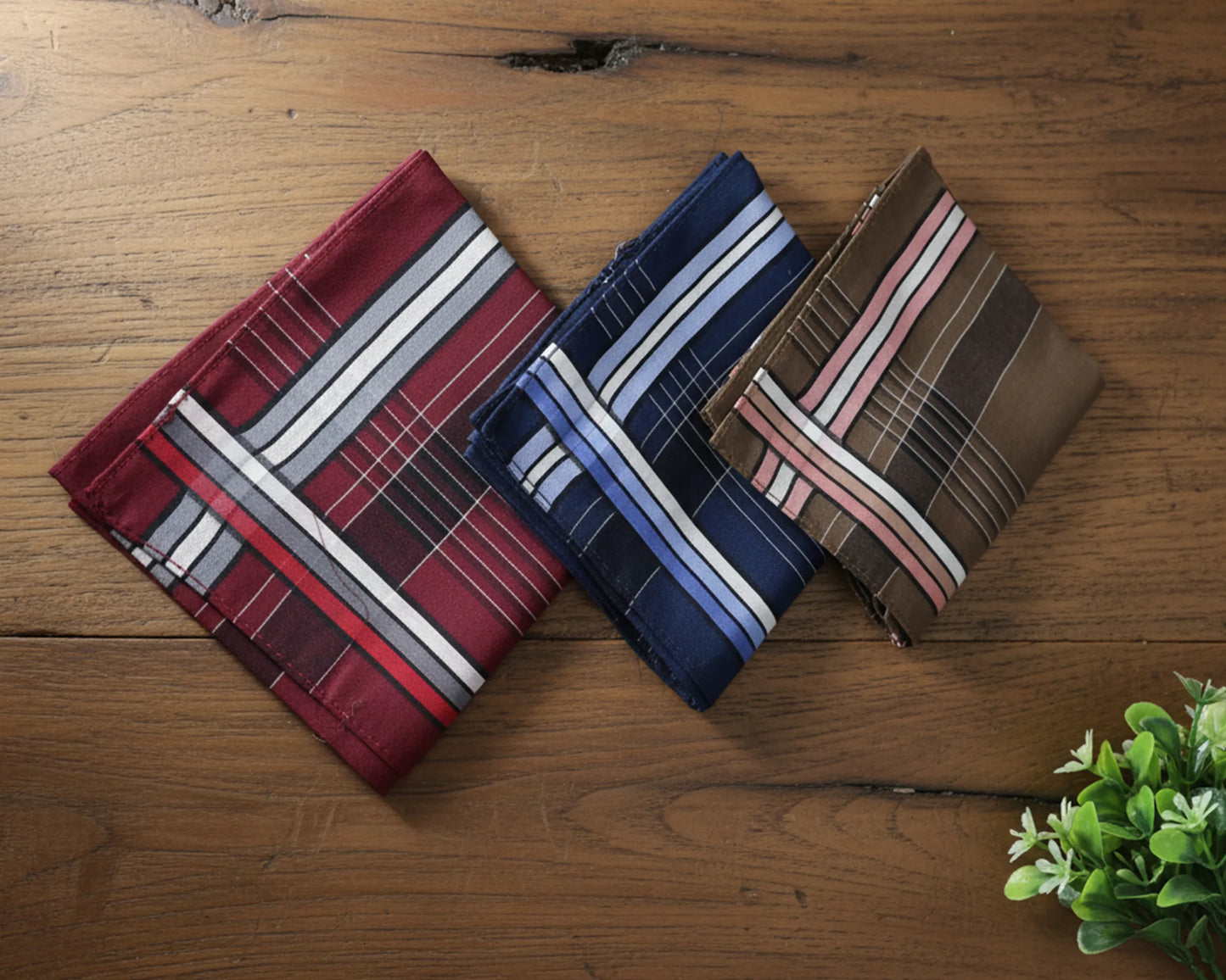 Three striped pocket squares on a wooden surface with a plant in the corner.