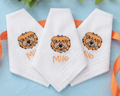 Three white handkerchiefs with lion embroidery and names embroidered on a blue background.