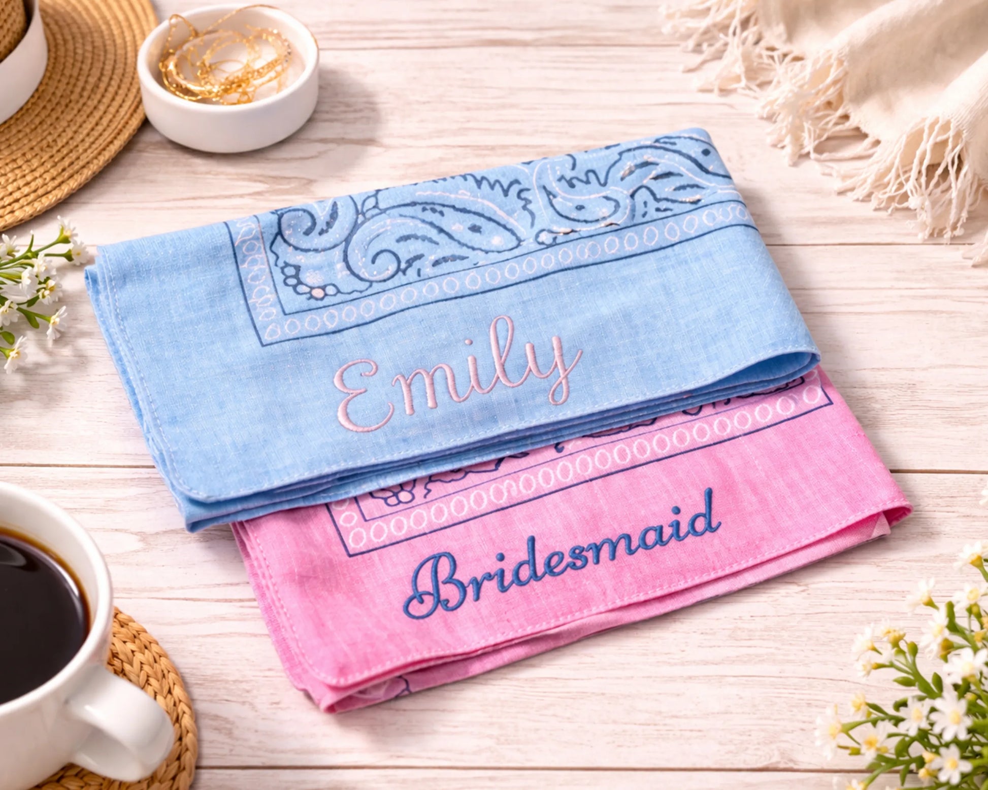 Two embroidered handkerchiefs, one blue and one pink, on a wooden surface with a cup of coffee and flowers.