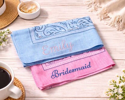 Two embroidered handkerchiefs, one blue and one pink, on a wooden surface with a cup of coffee and flowers.