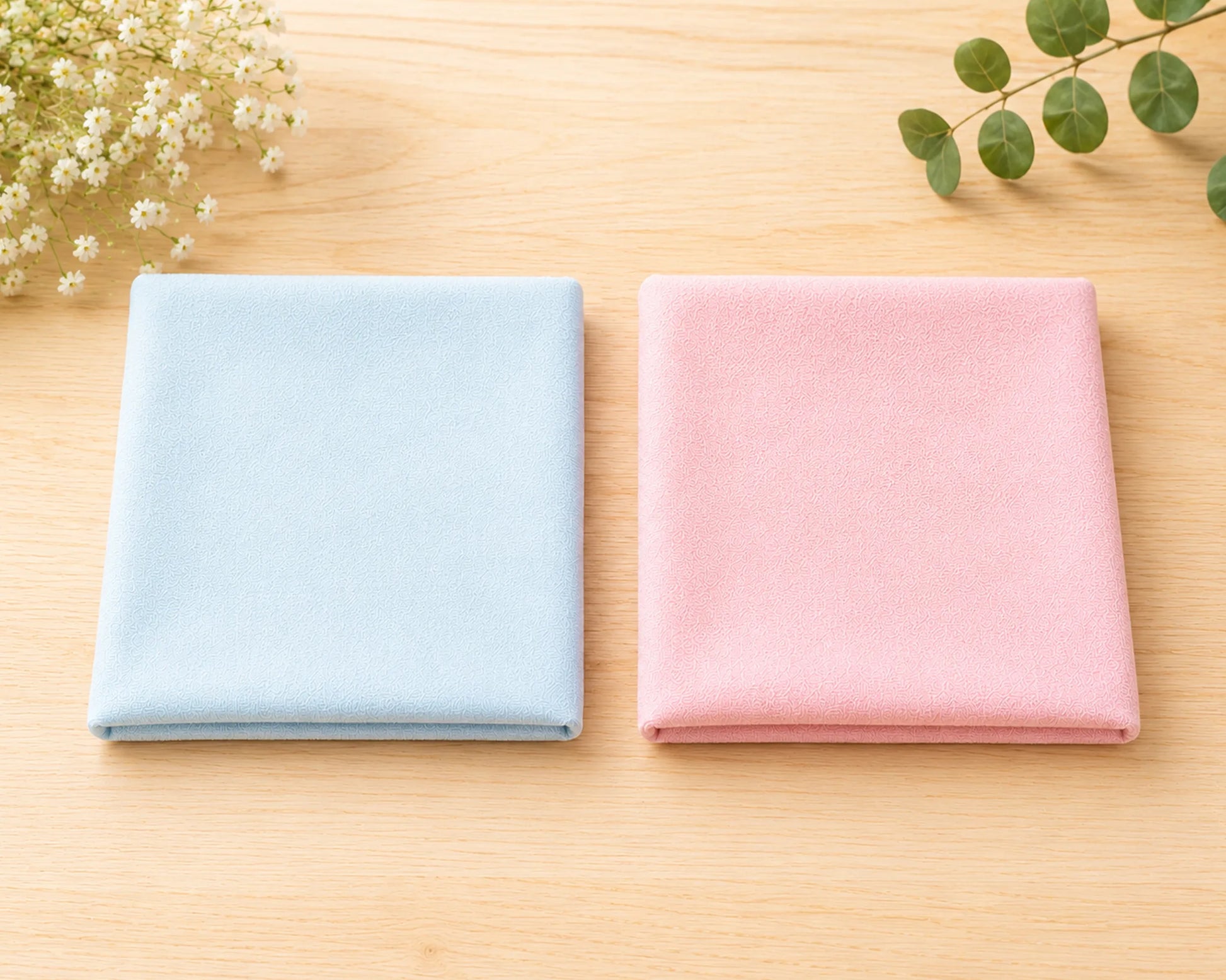 Two folded hanky, one blue and one pink, on a wooden surface with decorative elements.