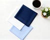 Two folded hanky, one blue and one white, on a white surface with a cup of coffee and a small plant.