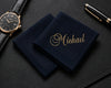 Two navy blue hanky with 'Michael' embroidered on them, a watch, and pen on a dark surface.