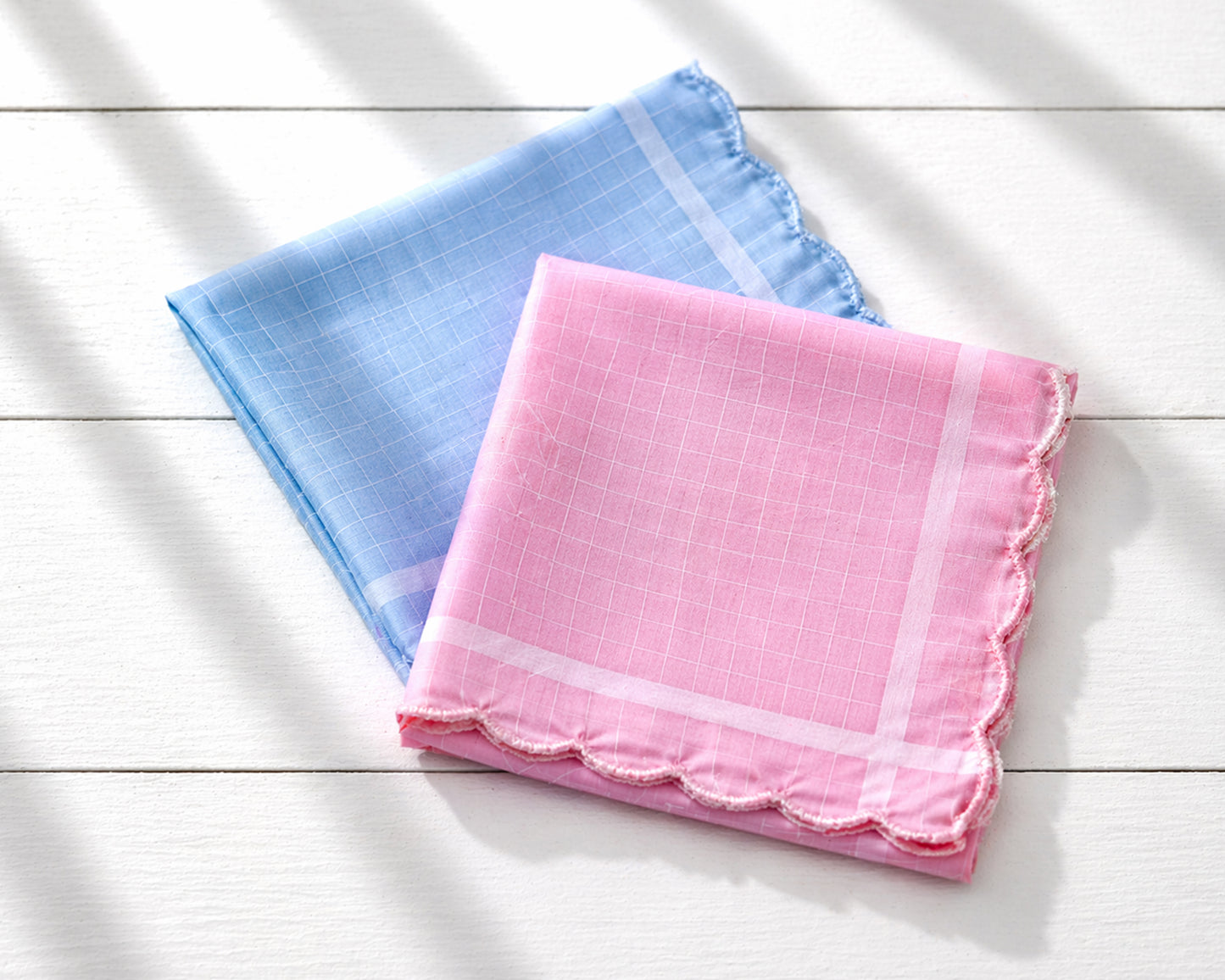 Two square handkerchiefs, one pink and one blue, on a light wooden surface.
