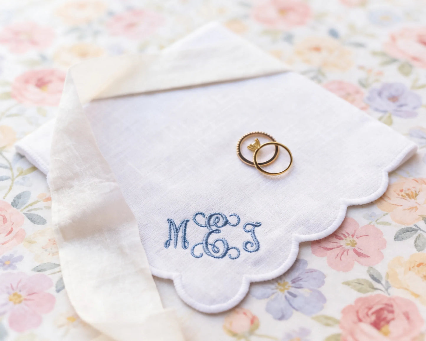 Two wedding rings on a embroidered handkerchief with 'MEJ' on a floral background