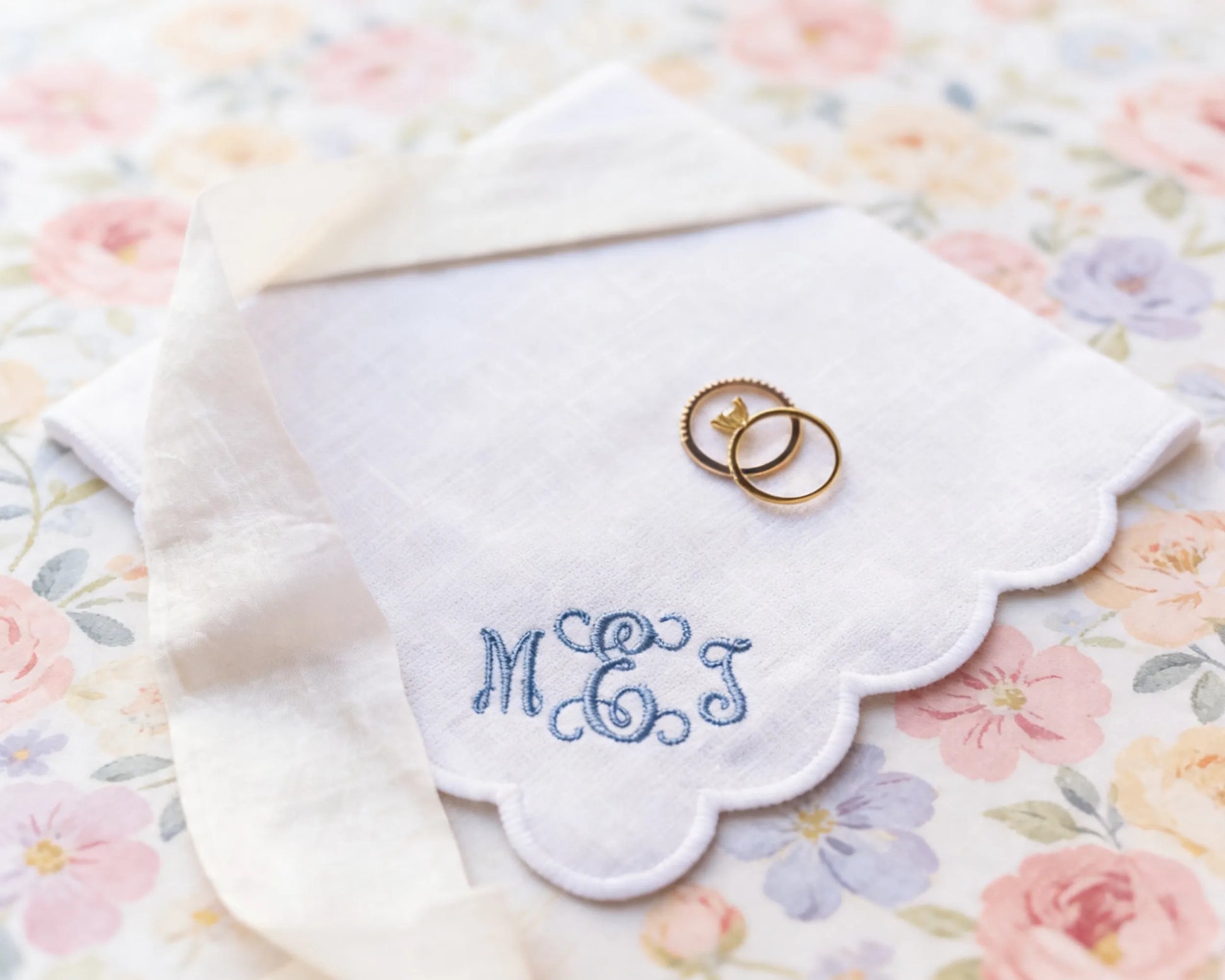 Two wedding rings on a embroidered handkerchief with 'MEJ' on a floral background