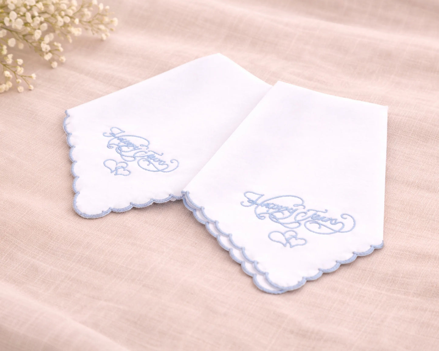 Two white handkerchiefs with blue embroidery on a beige surface.