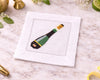 White cocktail napkin with a green and gold bottle design on a marble surface.