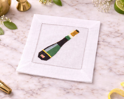White cocktail napkin with a green and gold bottle design on a marble surface.