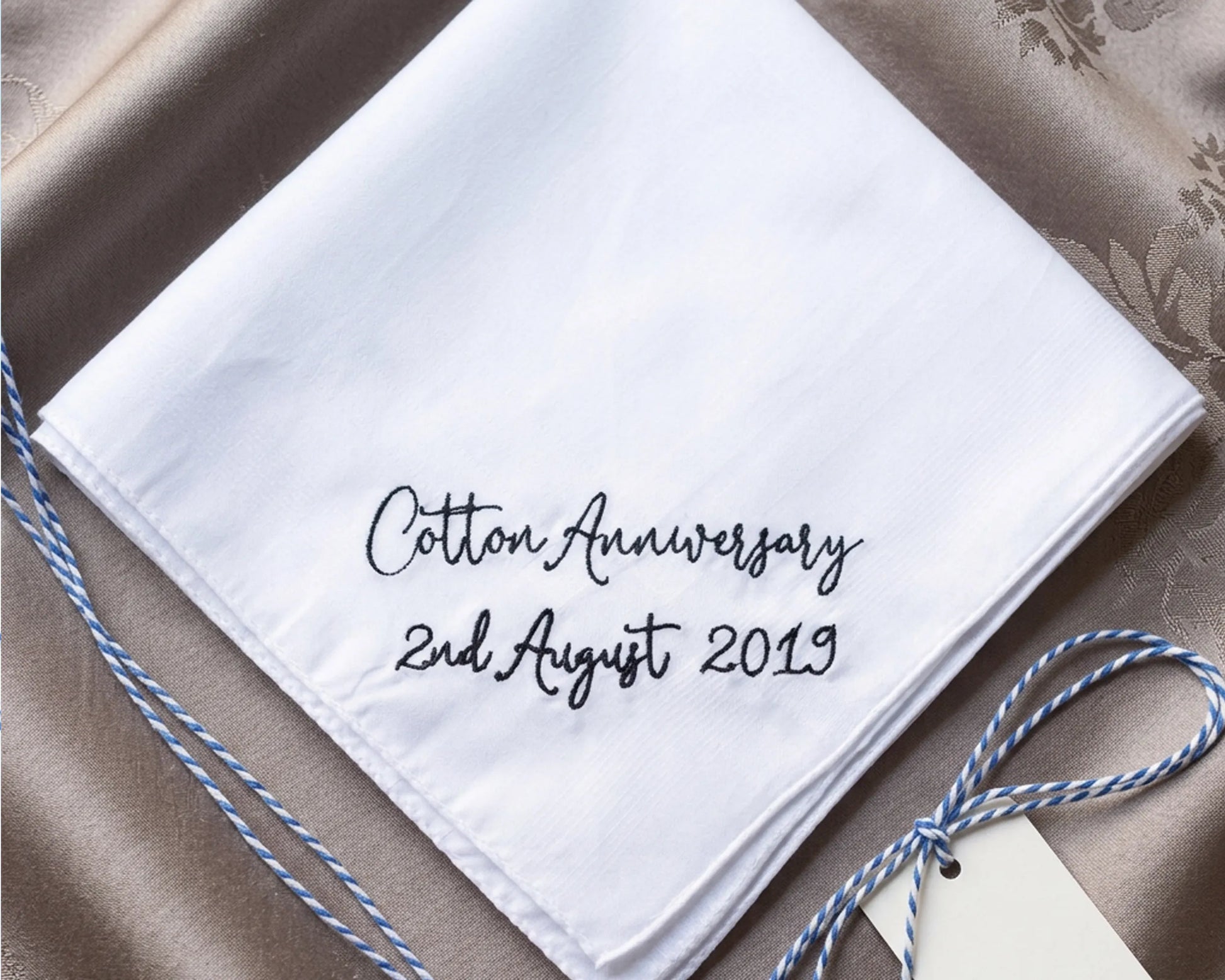 White handkerchief with 'Cotton Anniversary 2nd August 2019' text on a textured surface.