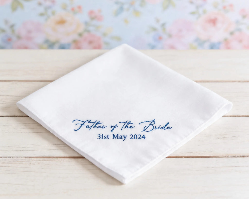 White handkerchief with 'Father of the Bride' text on a wooden surface with floral background