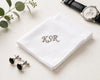 White handkerchief with 'KSR' embroidery, cufflinks, and a watch on a light surface.