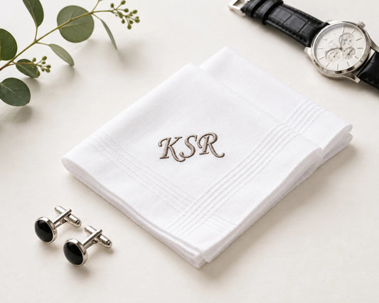 White handkerchief with 'KSR' embroidery, cufflinks, and a watch on a light surface.