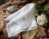 White handkerchief with a blue heart embroidery on a patterned fabric background with pearls and a flower.