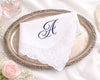 White handkerchief with a blue monogram 'A' on a decorative silver tray with flowers in the background.