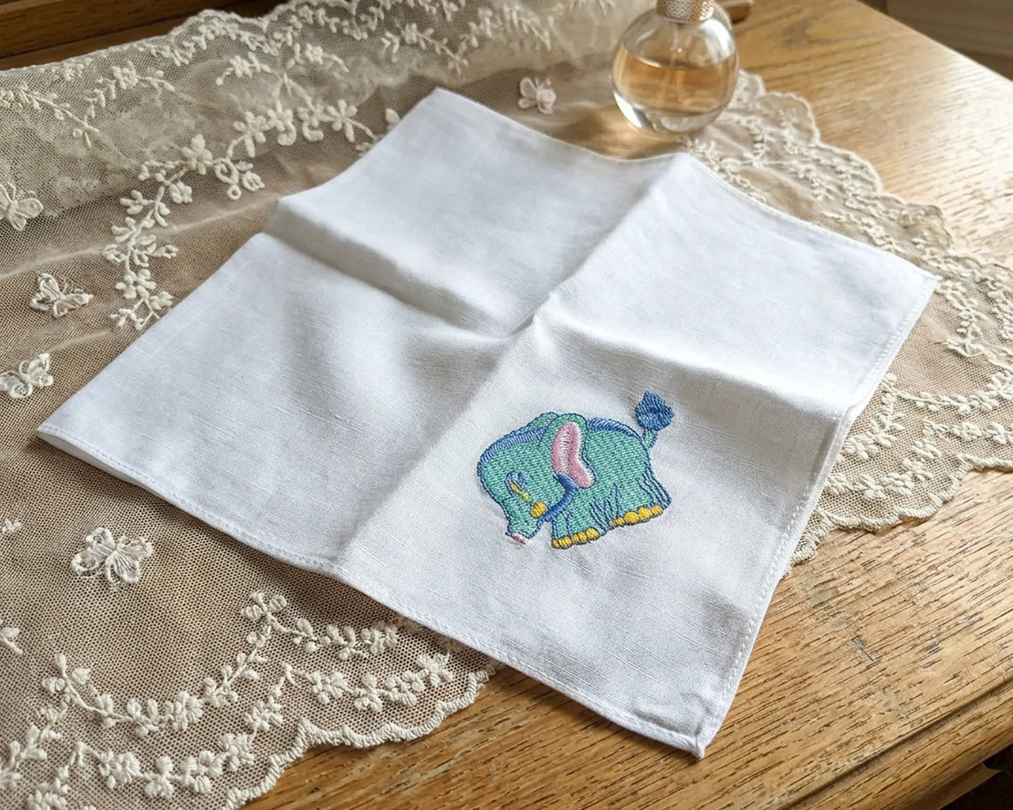 White handkerchief with a embroidered elephant design on a lace tablecloth.
