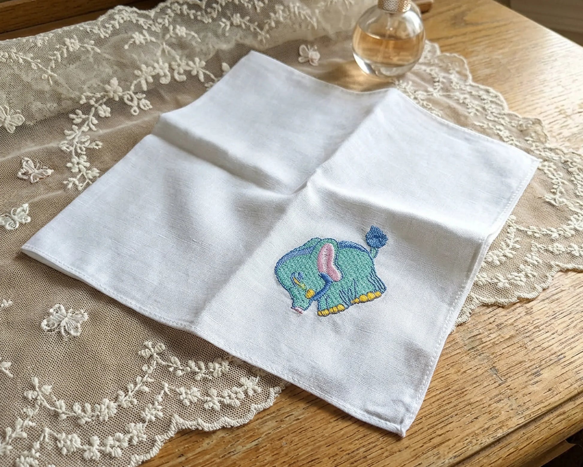 White handkerchief with a embroidered elephant design on a lace tablecloth.